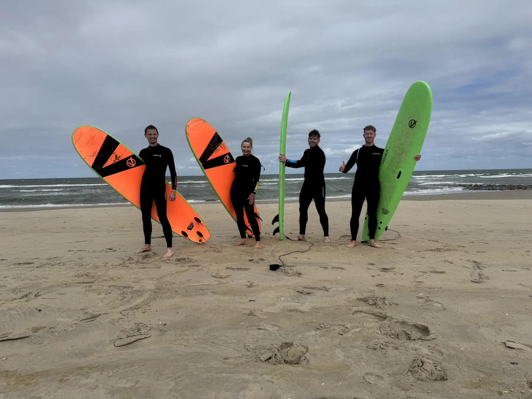 Vier surfers staan op het strand met hun surfplanken.